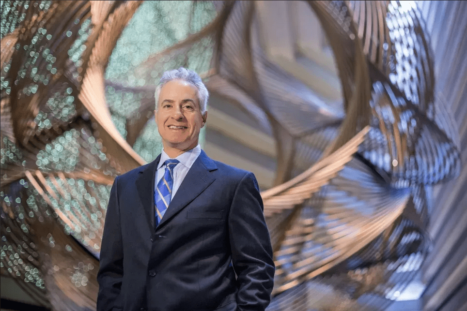 A man in suit and tie standing next to an abstract sculpture.